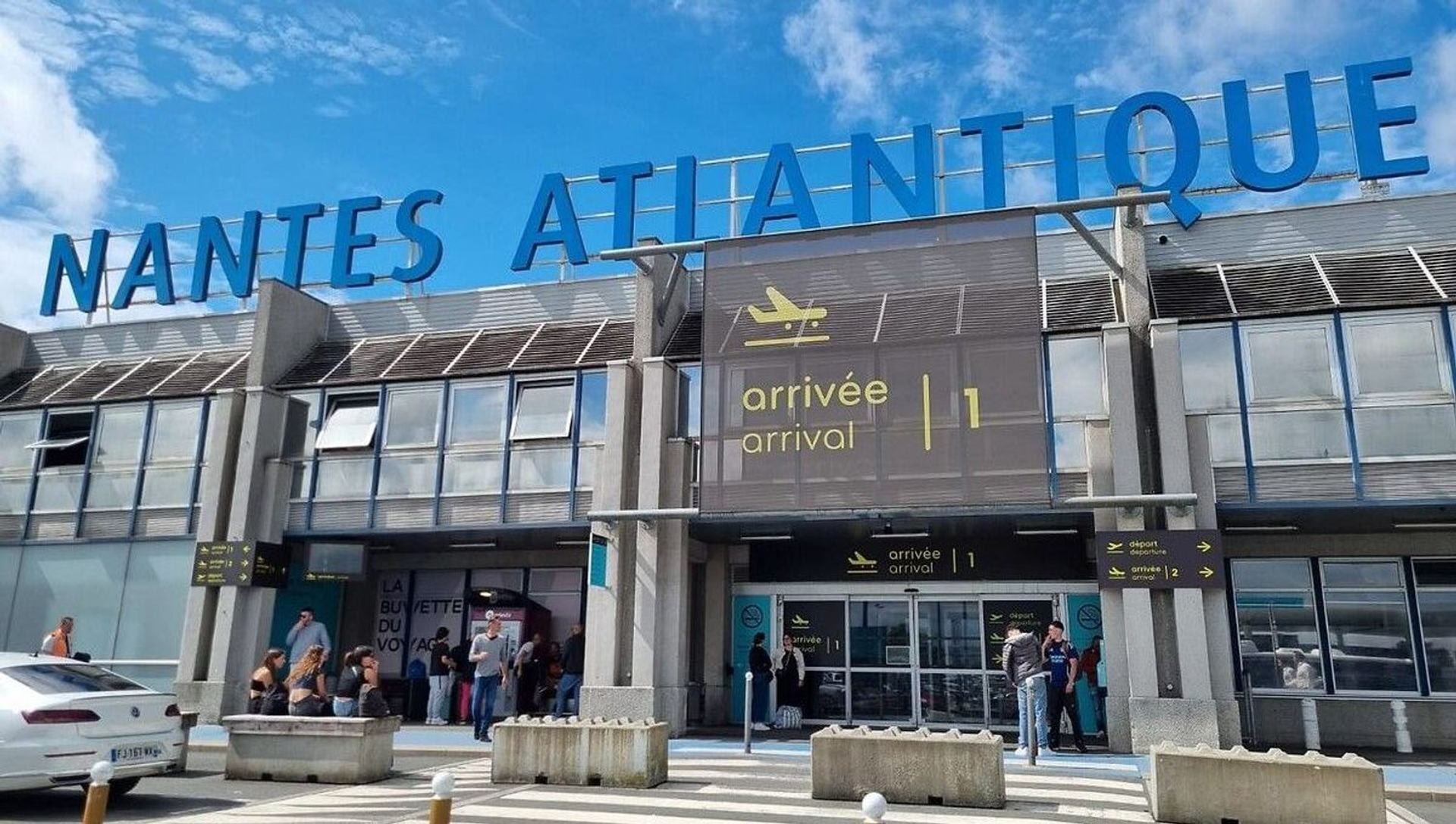 Façade de l'aérogare Nantes Atlantique avec voyageurs devant les portes d'arrivée